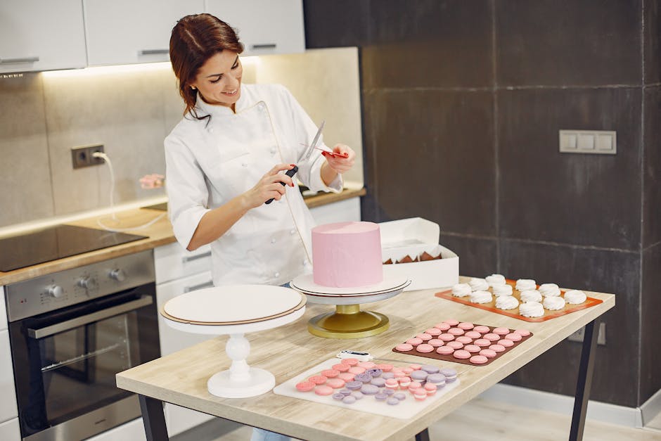 Cheerful female pastry cook in white apron standing in front of cake macaroons and sweets and sharpening knife and scissors in kitchen