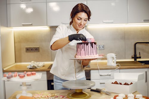 Smiling female cook decorating cake with delicious macaroons in modern restaurant