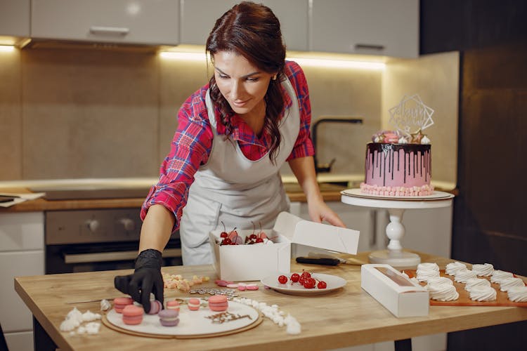 Focused Woman Decorating Cake With Macaroons In Kitchen