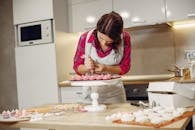 Woman in Red Long Sleeve Shirt and White Apron Icing Cookies