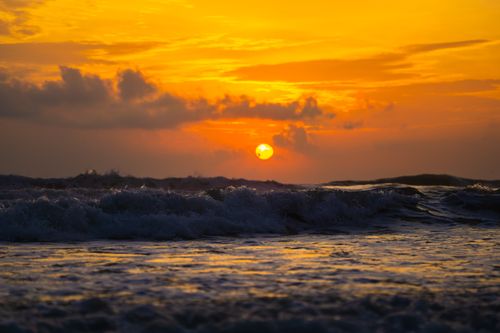 Free Breathtaking sunset over ocean waves with vibrant orange and yellow sky. Stock Photo