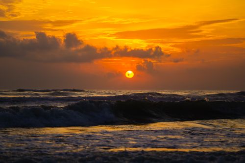 Free Captivating sunset over ocean waves, with a bright orange sky and silhouetted clouds, creating a dramatic seascape. Stock Photo