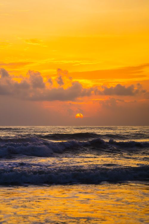 Free Breathtaking sunset over the ocean with vibrant orange sky and gentle waves. Stock Photo