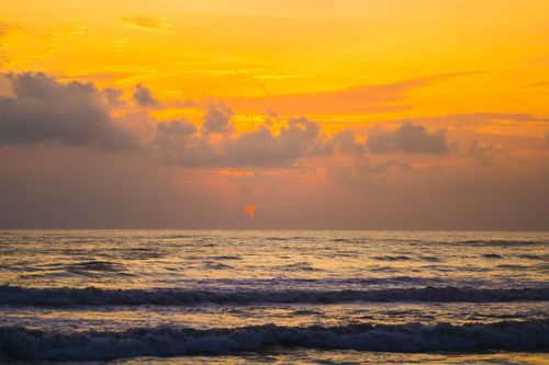 Free A serene ocean scene captured during sunrise with vibrant yellow and orange sky, reflecting over calm waters. Stock Photo