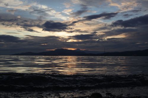 Free Serene sunset over the ocean with dramatic clouds and distant mountains. Stock Photo