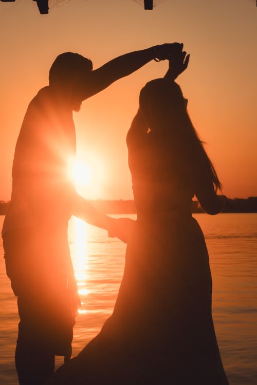 Free Silhouetted couple dancing by the water at sunset, evoking romance and serenity. Stock Photo