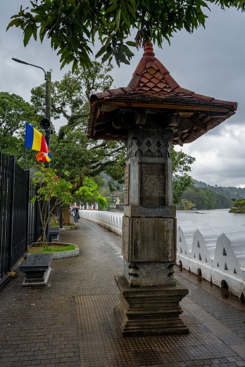 Free Scenic view of a riverside pathway in Kandy, Sri Lanka with cultural flags and traditional architecture. Stock Photo