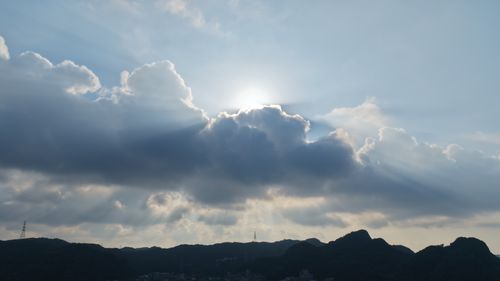 Free Clouds with sun rays create a dramatic scene over mountains at sunset, ideal for weather-focused content. Stock Photo