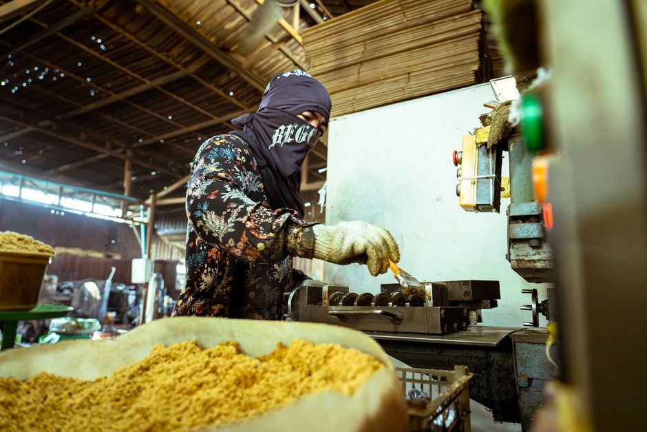 Masked worker operating machinery in an industrial factory setting, processing materials.