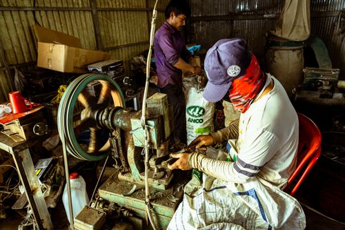 Free Two men engaged in metalwork inside a workshop, with visible machinery and tools around. Stock Photo