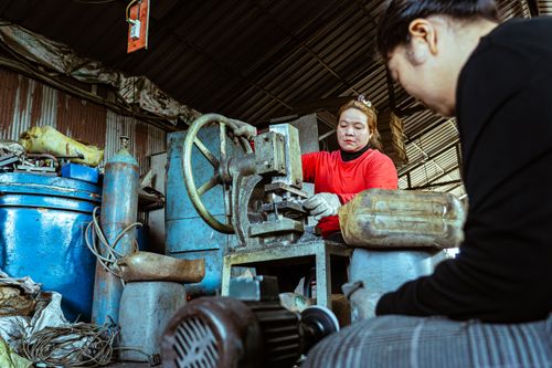 Free Two women focused on machinery work in a cluttered industrial workshop filled with equipment. Stock Photo
