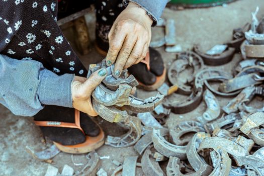 A person sorting metal parts for recycling, focusing on hands with dirt and wear.