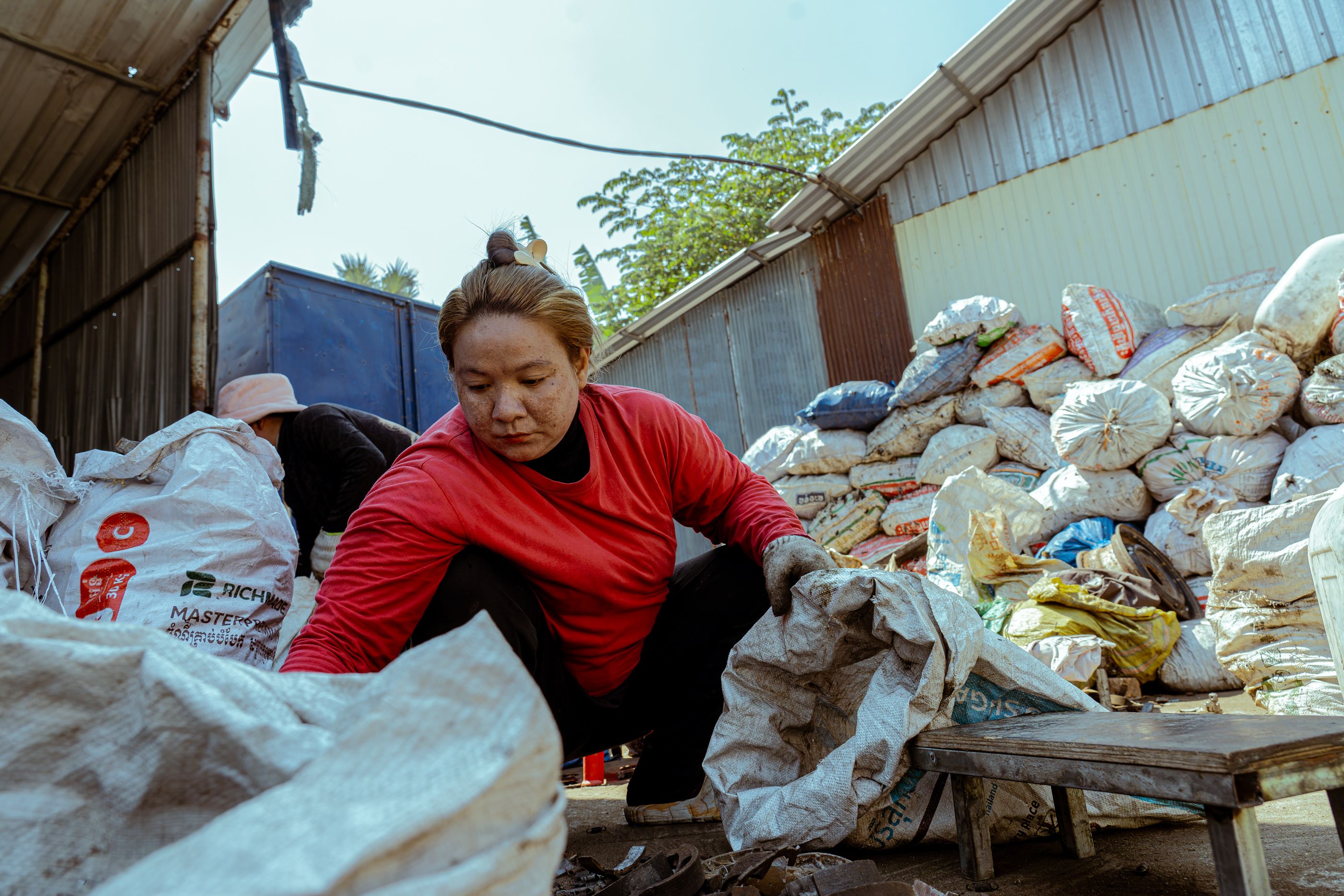 Woman sorting bags of recyclable material at an outdoor industrial site