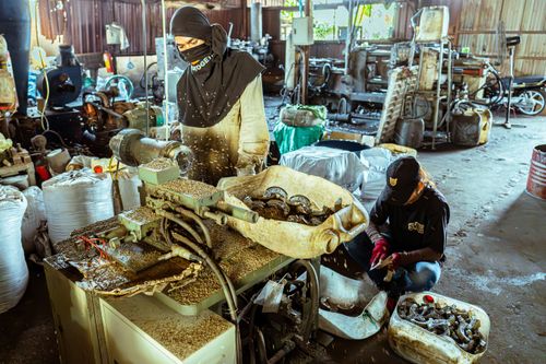 Free Two workers operate machinery in a cluttered industrial workshop, processing metal parts. Stock Photo