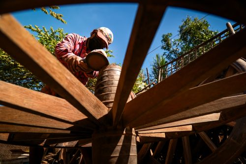 Free A skilled craftsman in a hat and mask working on a traditional wooden cart wheel outdoors. Stock Photo
