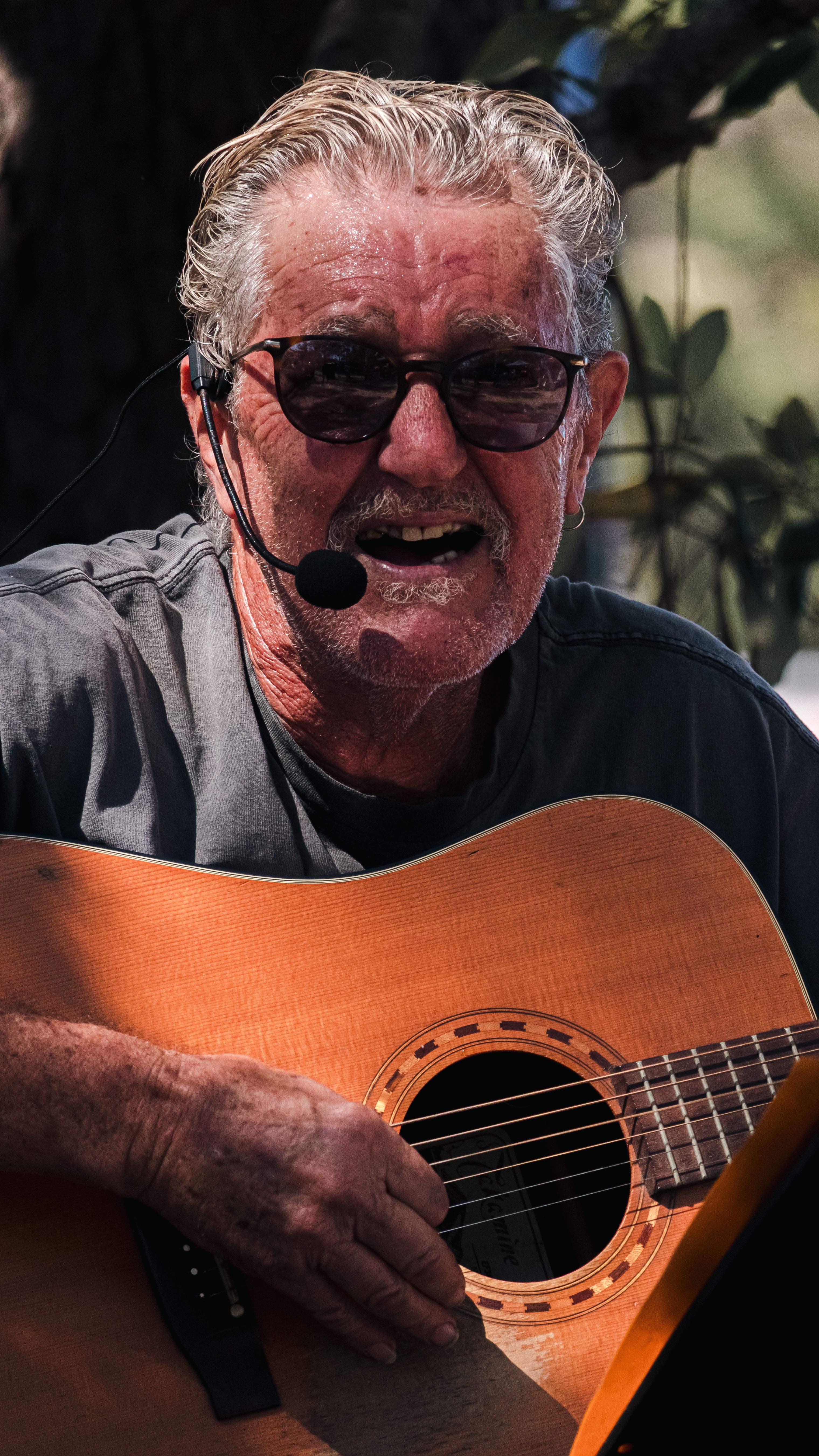 Senior male musician playing acoustic guitar with mic outdoors. Passionate performance.