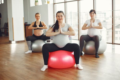 Positive young pregnant women practicing yoga in modern studio