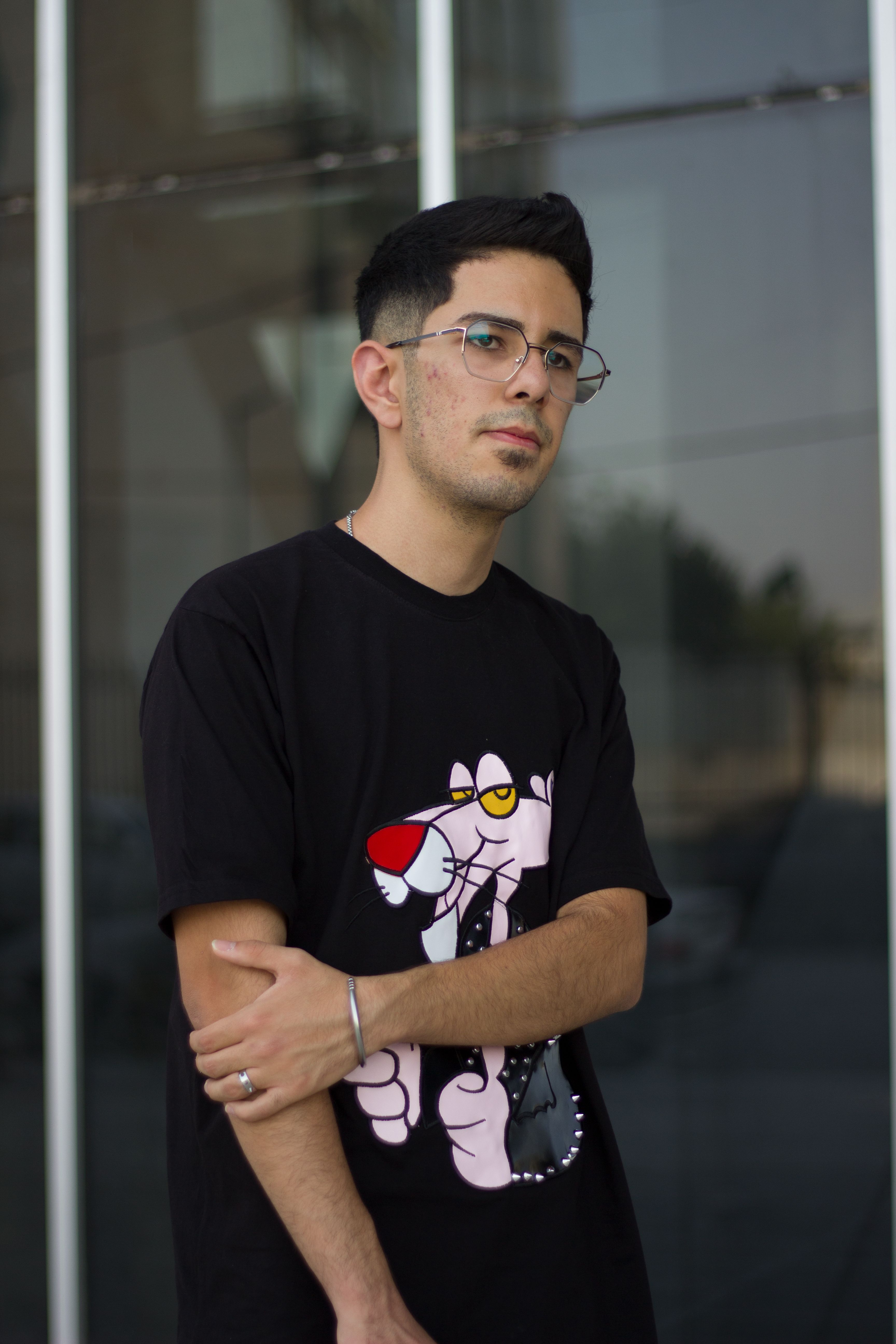 Portrait of a young Middle Eastern man in a graphic T-shirt, standing outdoors in Kermanshah, Iran.