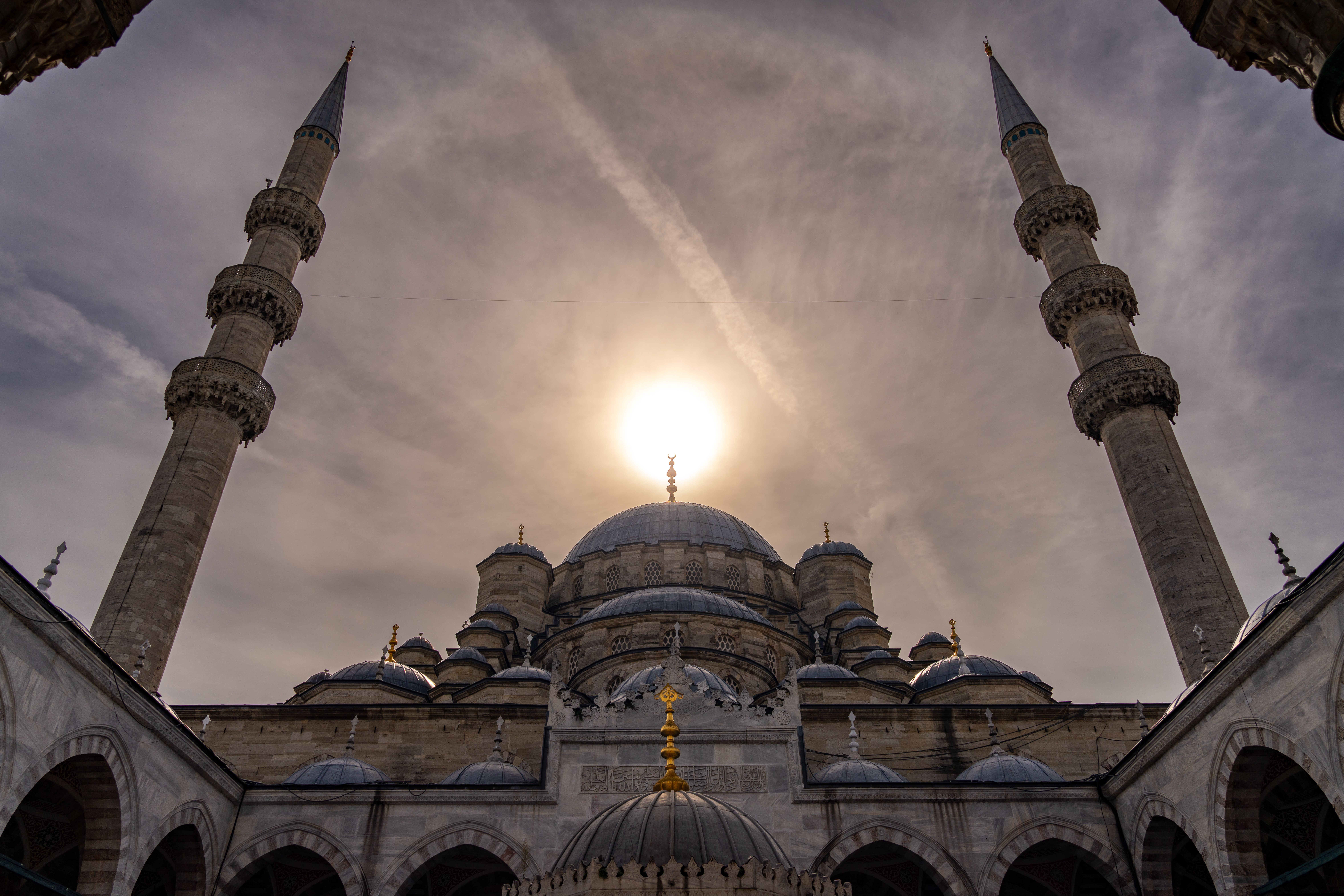Dramatic architectural photo of the New Mosque with the sun behind it in Istanbul, Türkiye.
