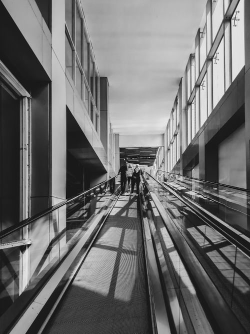 Free Black and white photo capturing a modern escalator in Jakarta's airport with people ascending. Stock Photo