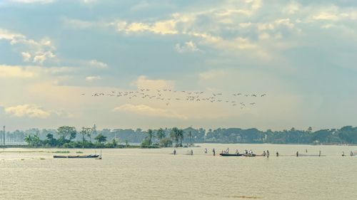 Free Peaceful landscape of a lake in Bangladesh with birds flying overhead and distant fishermen at work. Stock Photo
