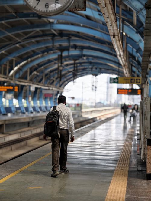 Free Man walking on a deserted train platform under a blue arched roof, suggesting urban travel. Stock Photo