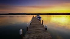 宁静的湖面上，日出静谧，木制码头和船只倒映在平静的湖水中