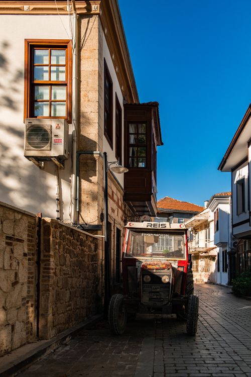 Free A rustic tractor parked on a narrow cobblestone street in a historic village under a clear blue sky. Stock Photo