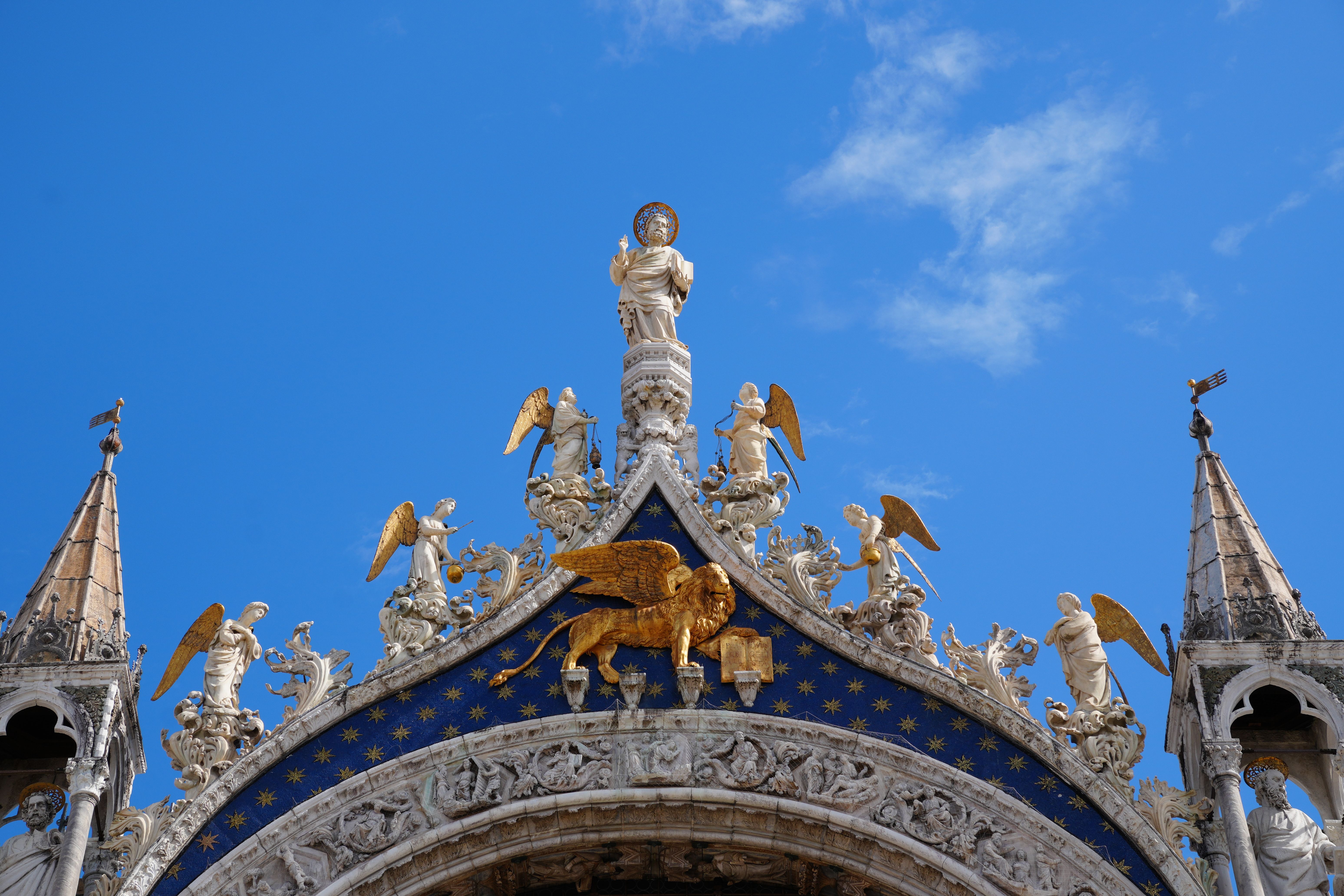 A detailed view of the ornate, angel-adorned facade of St. Mark's Basilica in Venice under a clear blue sky.