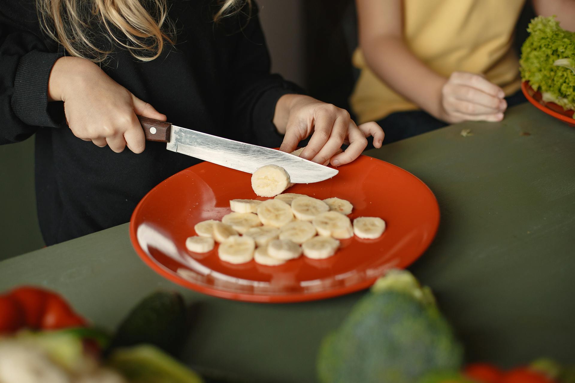 Woman in Black Shirt Slicing Banana on Red Round Plate