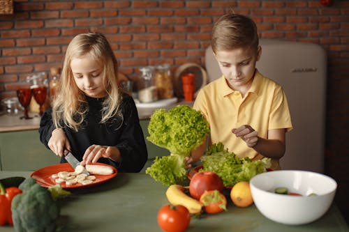 Free Adorable children cutting with knife while preparing healthy food together Stock Photo