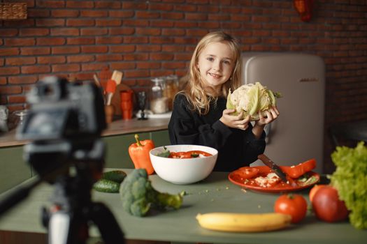 A young girl holds a cauliflower while making a fresh vegetable salad in a kitchen.
