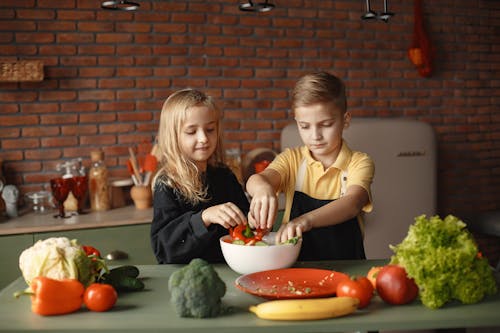 Little friends preparing vegetable salad together in kitchen at home
