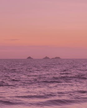 Peaceful ocean scene at sunset with pink skies and distant islands.