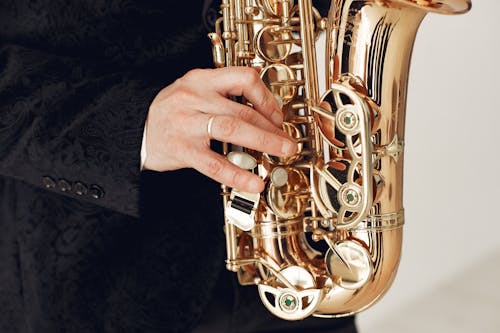 Unrecognizable talented male artist wearing concert costume playing jazz melody on saxophone standing against white background during rehearsal or music show