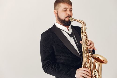Free Man in a black suit playing a saxophone in a studio setting, exuding elegance. Stock Photo