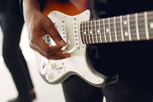 Unrecognizable young male musician playing electric guitar while standing near anonymous colleague on blurred background during celebration party or live music show