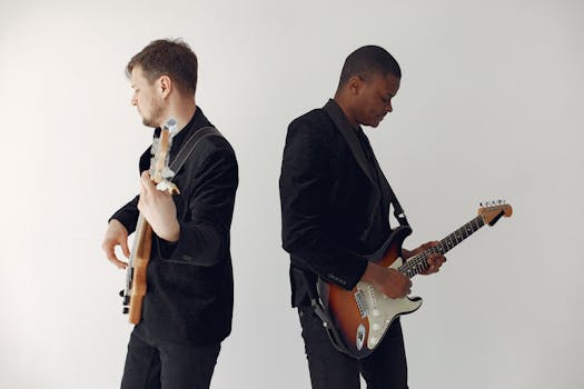 Two musicians in black suits perform with electric guitars in a studio setting.