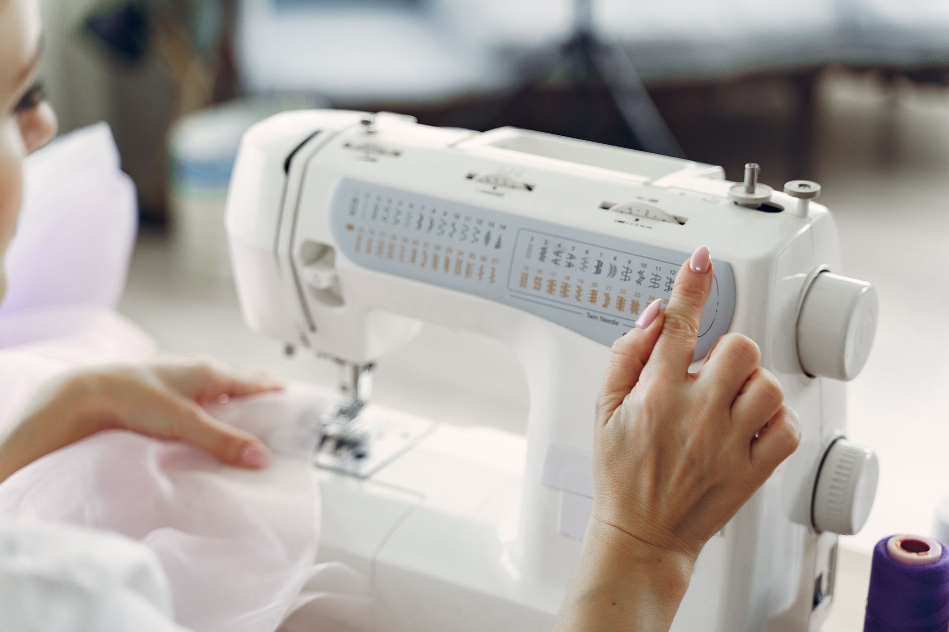 A person sewing with a white sewing machine, adjusting settings for precise tailoring.