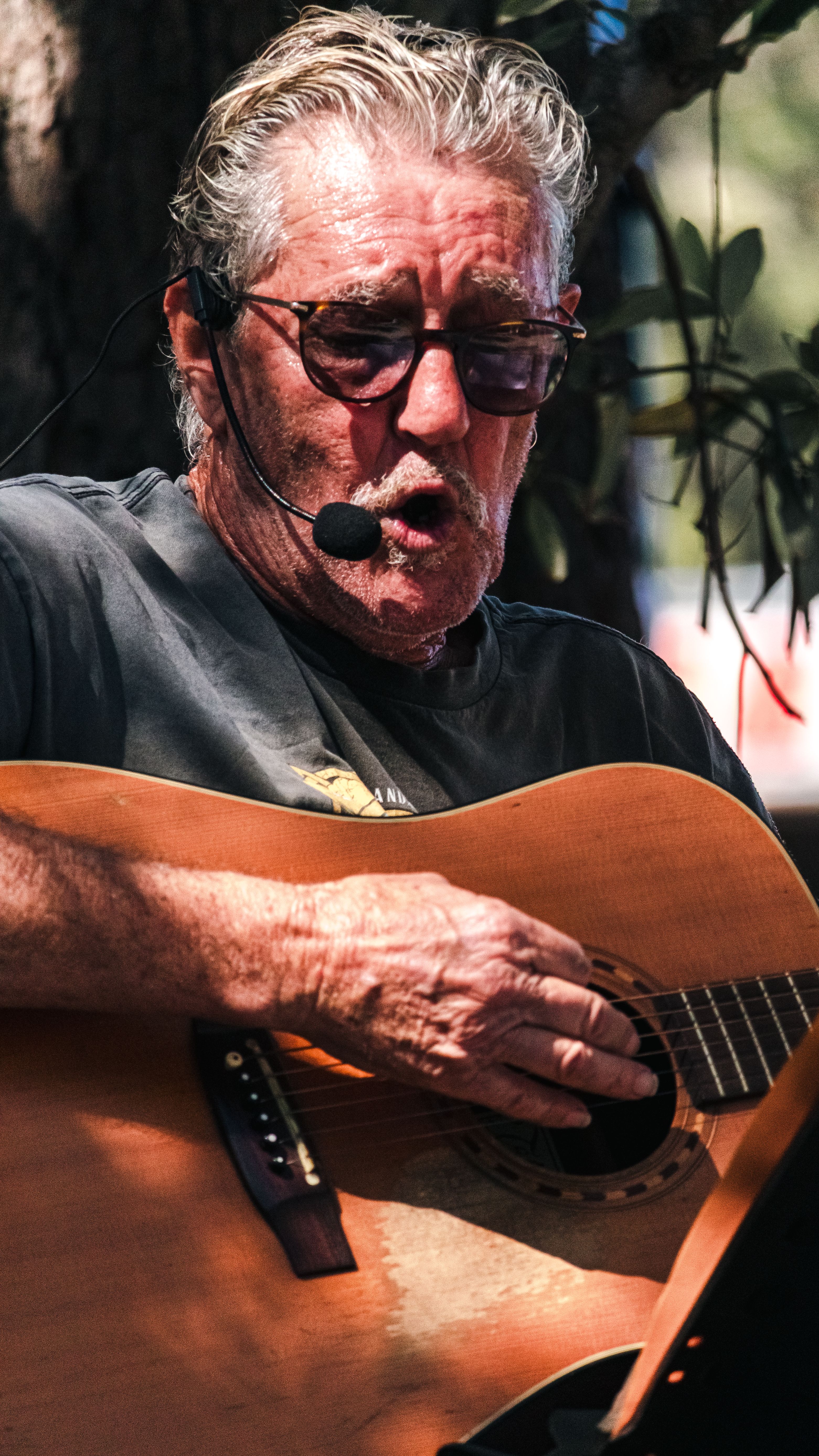 Senior male street performer singing and playing guitar outdoors in Seventeen Seventy, Australia.