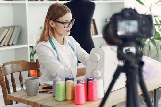 Fashion designer focused on sewing, surrounded by colorful threads and sewing tools in her studio.