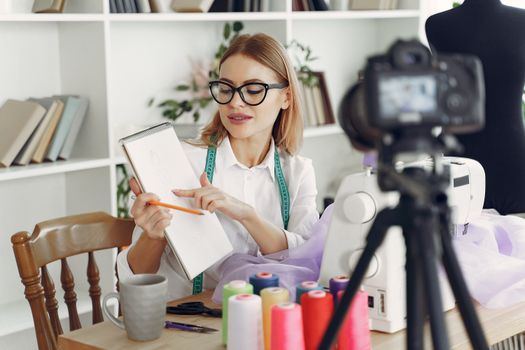 A fashion designer reviews sketches while working on a sewing project in a modern studio.