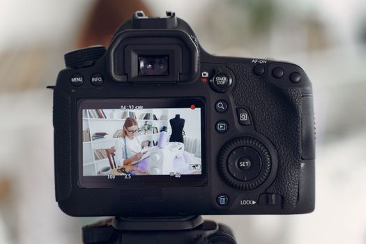 A professional seamstress works on a garment, recorded and displayed through a camera's viewfinder in a modern studio.