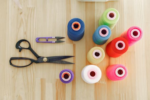 Top view of vibrant sewing threads and scissors on a wooden table, showcasing creativity and craft materials.