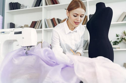 Young inspired seamstress sewing party dress in tailor atelier
