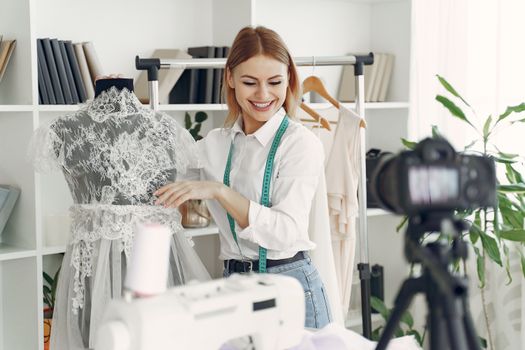 A fashion designer adjusting a dress on a mannequin while recording a video in a studio.