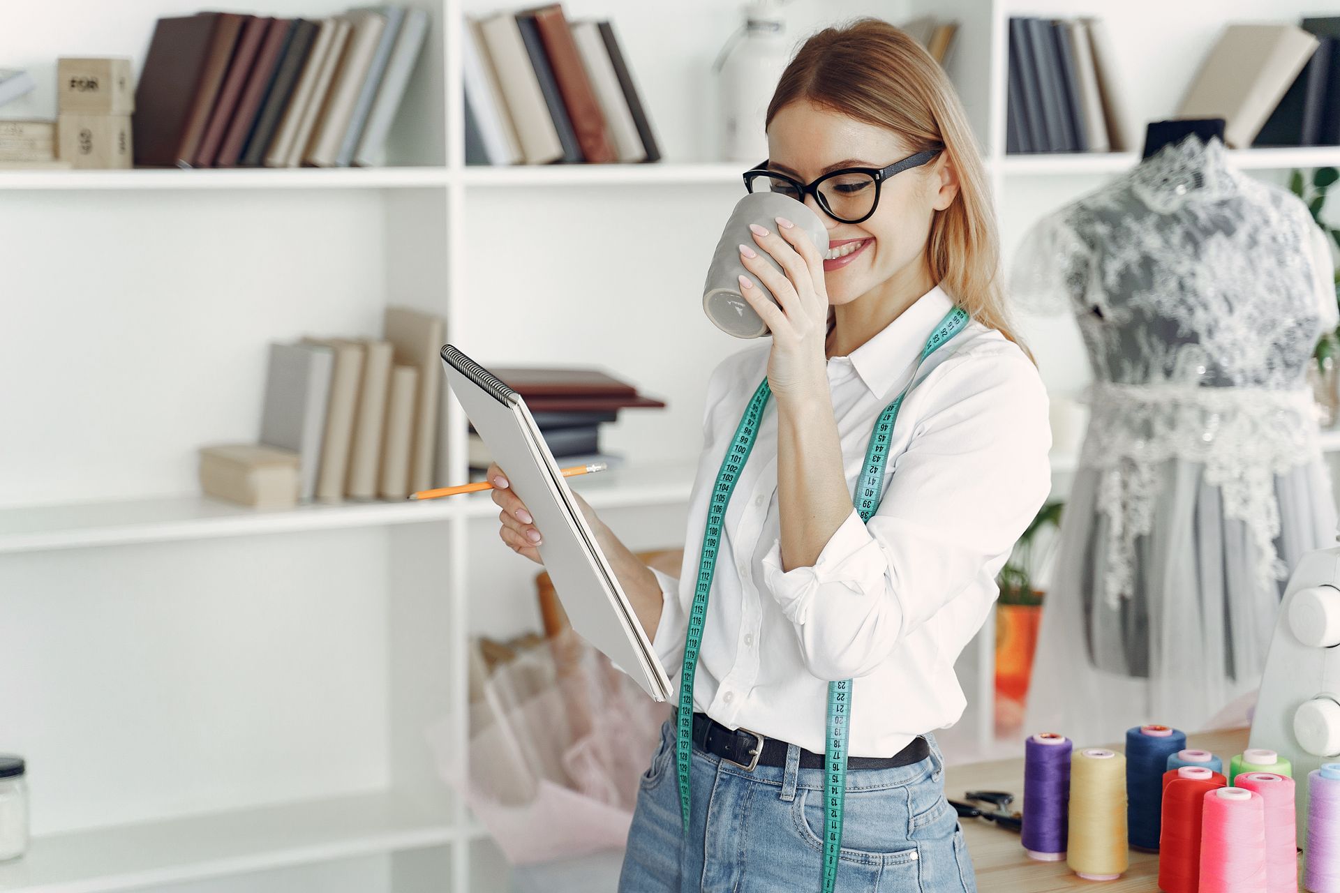 A fashion designer in a modern studio drinks coffee while working with fabrics and sketches.