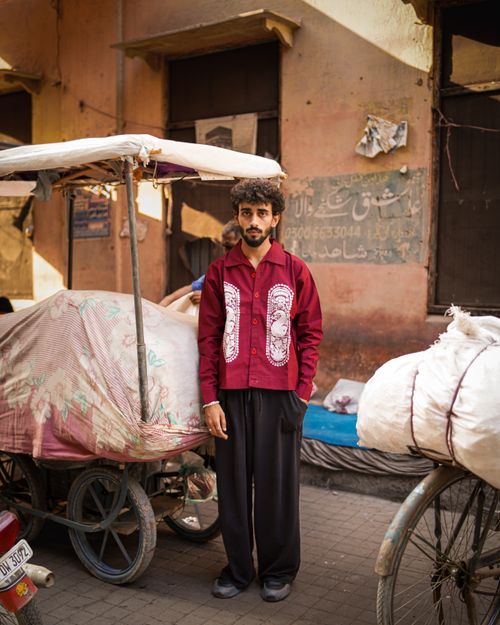 Free Portrait of a young man standing beside carts in a vibrant street market in Pakistan. Stock Photo