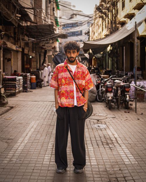Free Stylish young man with a guitar on his back standing confidently in a bustling Pakistani street market. Stock Photo