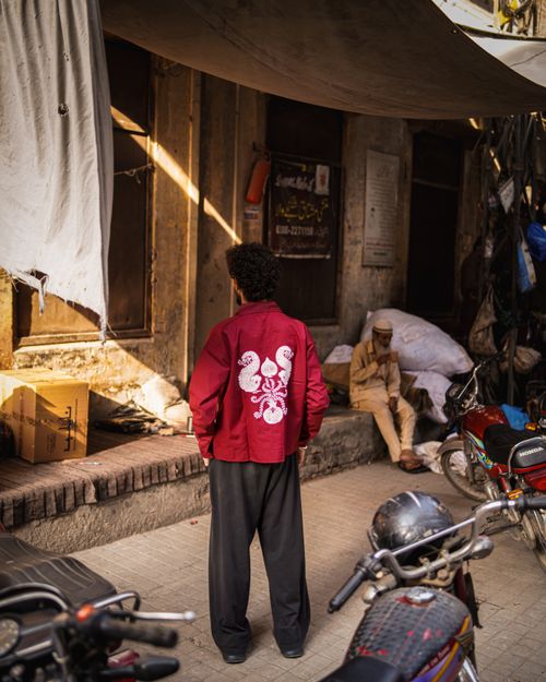 Free Urban street scene in Pakistan featuring a person in a red jacket and a seated man. Stock Photo